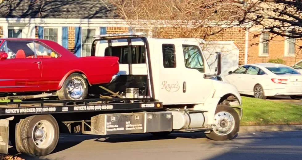 Royce's white rollback, the name in script on the cab door, carrying a red classic car past brick houses